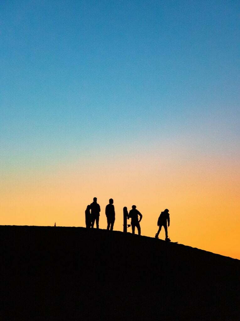 Silhouettes of travelers on a dune at sunset