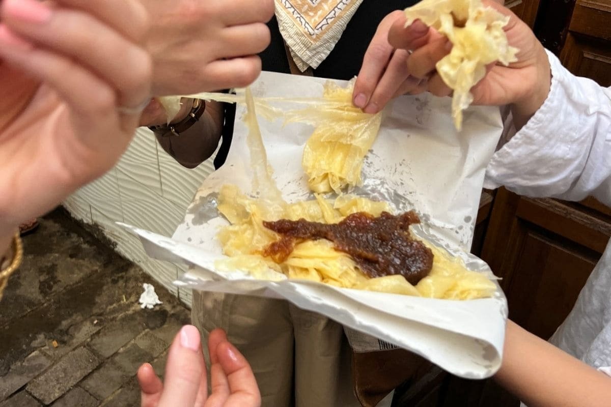 People share a paper tray of nachos with melted cheese and a dark brown topping as several hands reach in to grab chips.