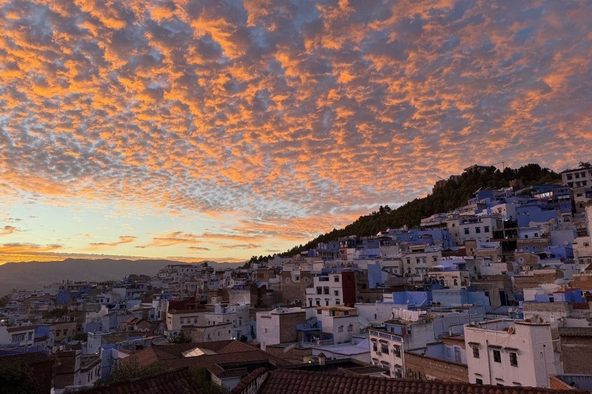 Sunset over a hillside town with blue and white houses and orange clouds above.