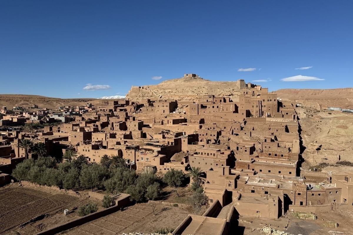 Adobe village built on a hillside under a clear blue sky, with a fortress atop the hill in the background.