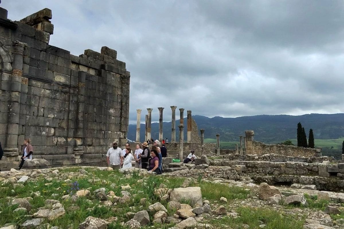 Group of tourists exploring ancient stone ruins with columns and hills in the distance.