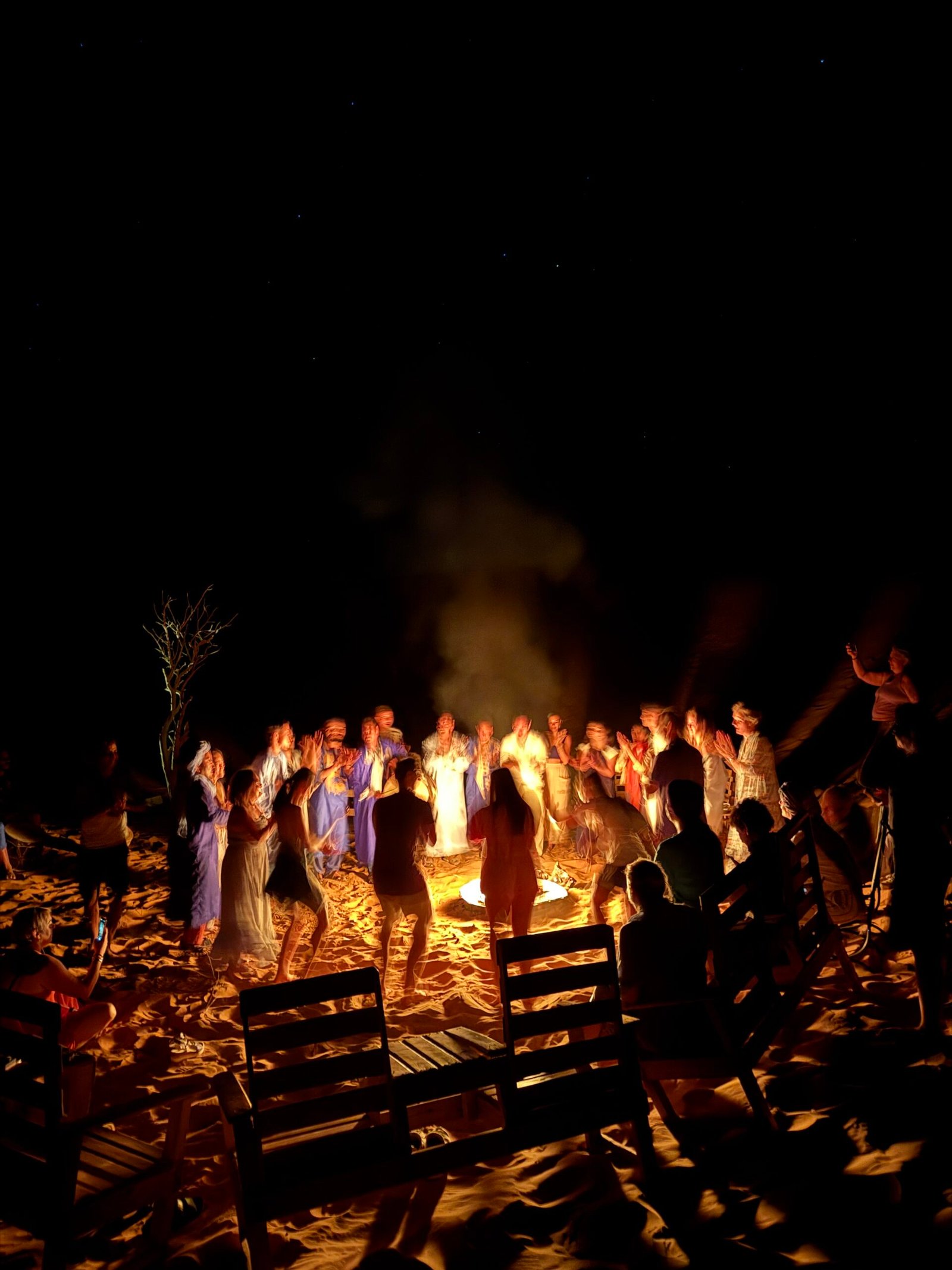 Travelers dancing around a bonfire in the Sahara desert at night