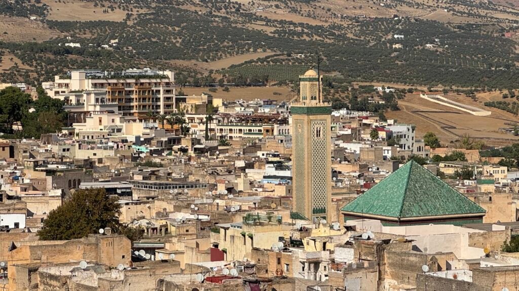 Fez medina rooftops with a minaret and green-tiled mosque roof